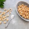 A bowl of cashews on a table next to a spoon of salt.