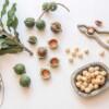 Roasted and Salted Macadamias in a bowl surrounded by shelled macadamias on a table next to a nutcracker